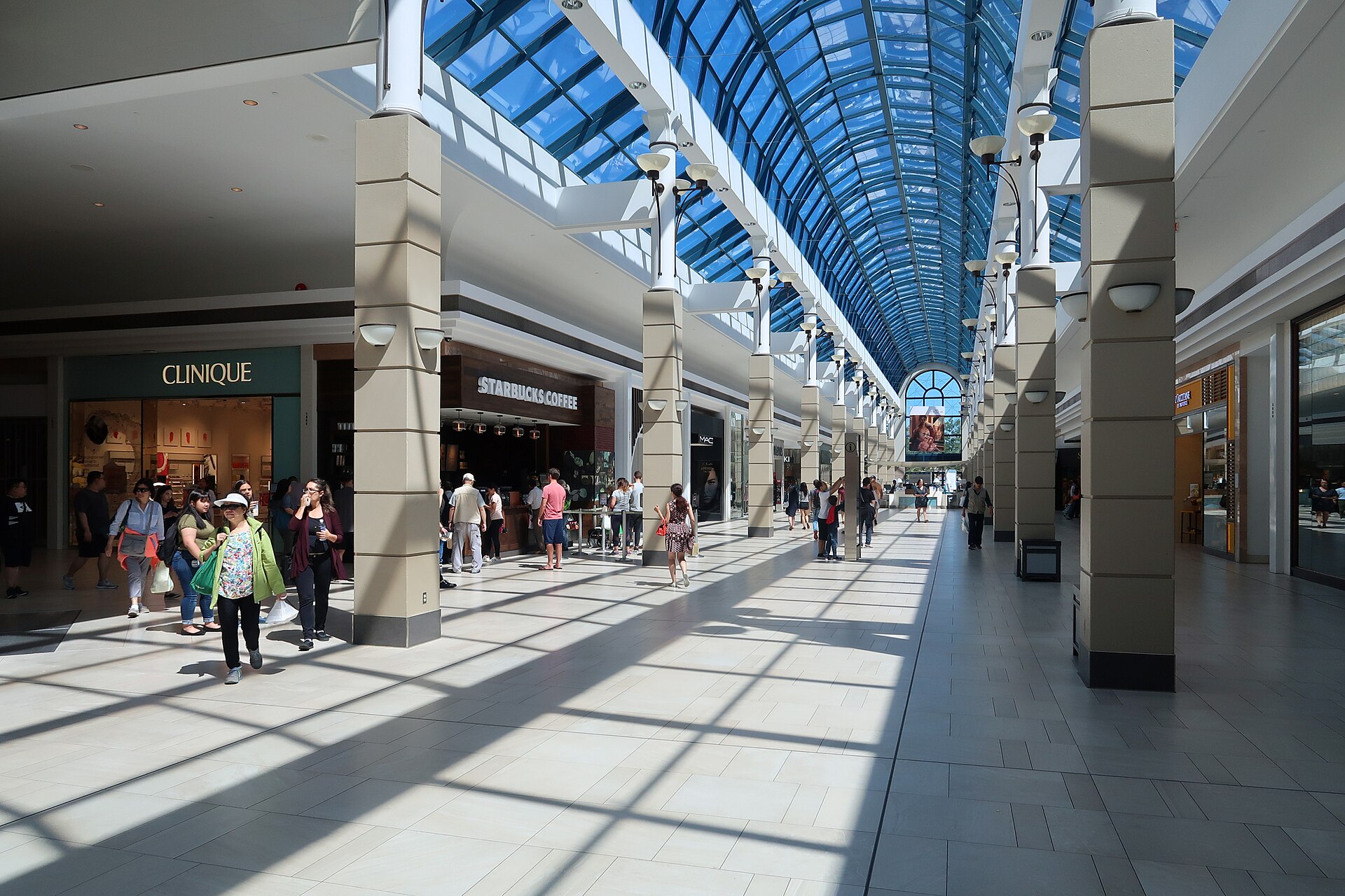 A sunlit glass-roofed galleria inside a shopping centre